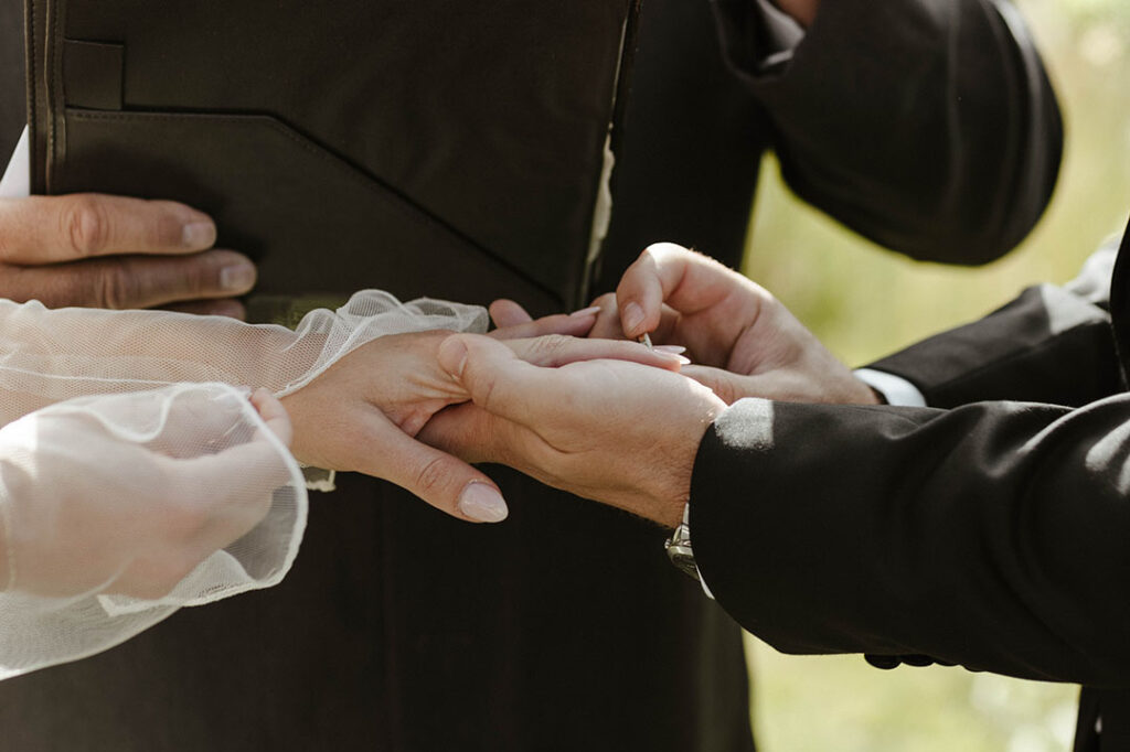 groom putting a ring on the brides finger during the ceremony at kinship ranch