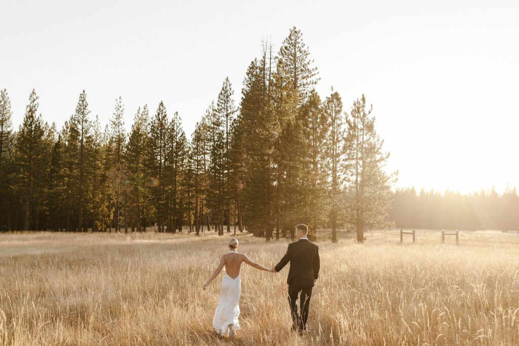 bride and groom walking into the sunset holding hands at their summer wedding at kinship ranch