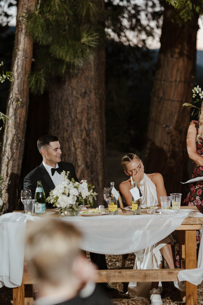 bride covering her face while the groom laughs during speeches at their summer wedding at kinship ranch