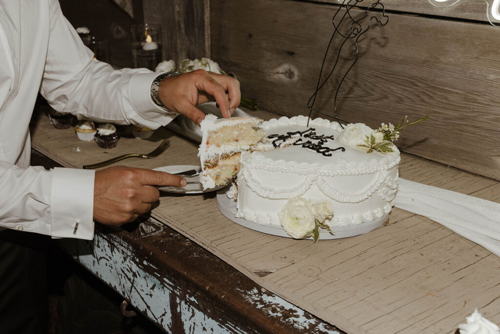 modern white wedding cake with piping and flowers at a summer wedding at kinship ranch being cut