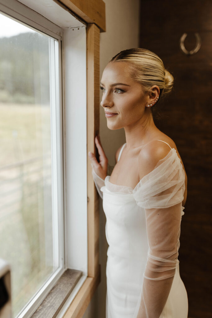 bride looking out the window before her summer wedding at kinship ranch