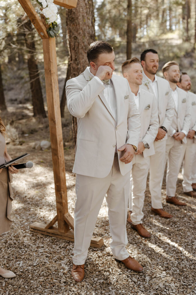Wedding groom emotional and wiping eye during wedding ceremony with groomsmen in background at the Corner Barn