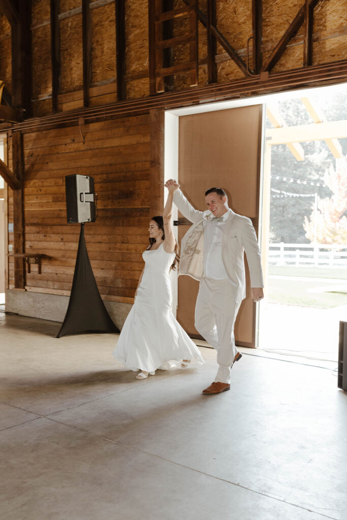 Wedding couple holding hands in air together during grand entrance at the Corner Barn