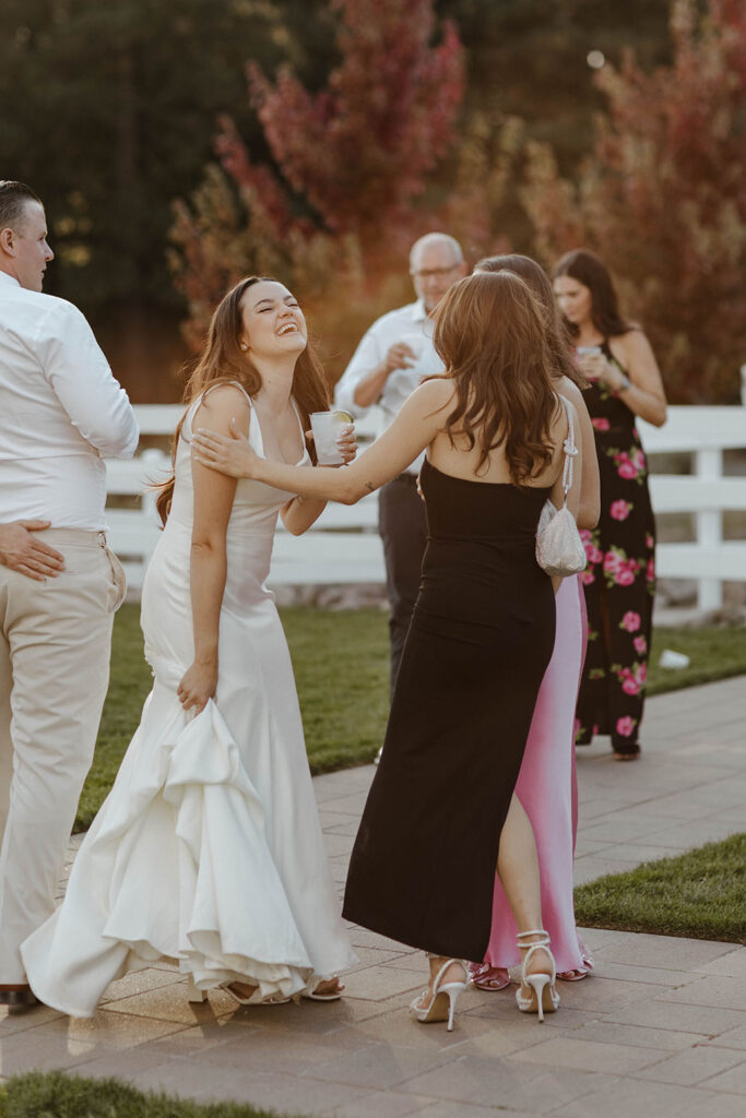 Wedding bride laughing with guests as she holds her dress with colorful trees in background at the Corner Barn