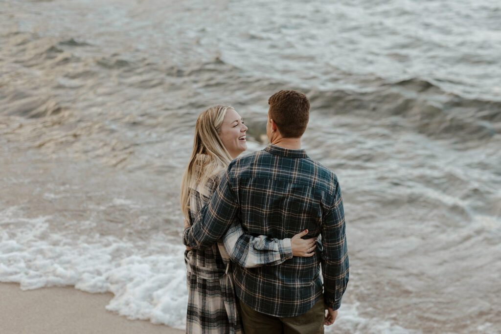 Woman with arm around husband laughing and smiling at him while standing at edge of Lake Tahoe