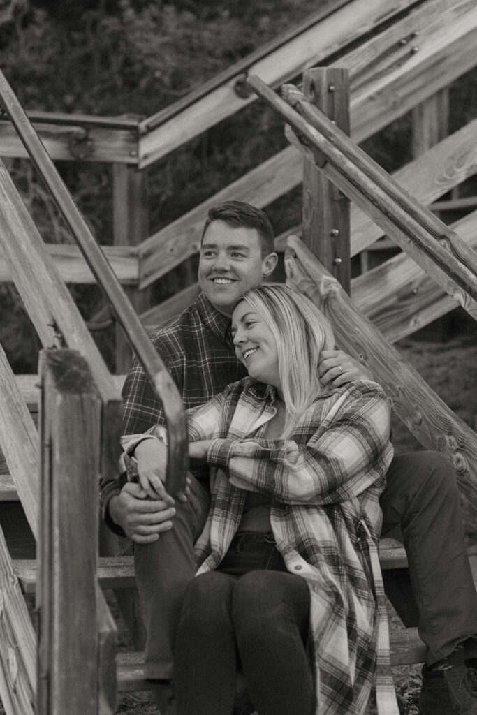 Married couple sitting on wooden staircase together as they smile and look out to Lake Tahoe