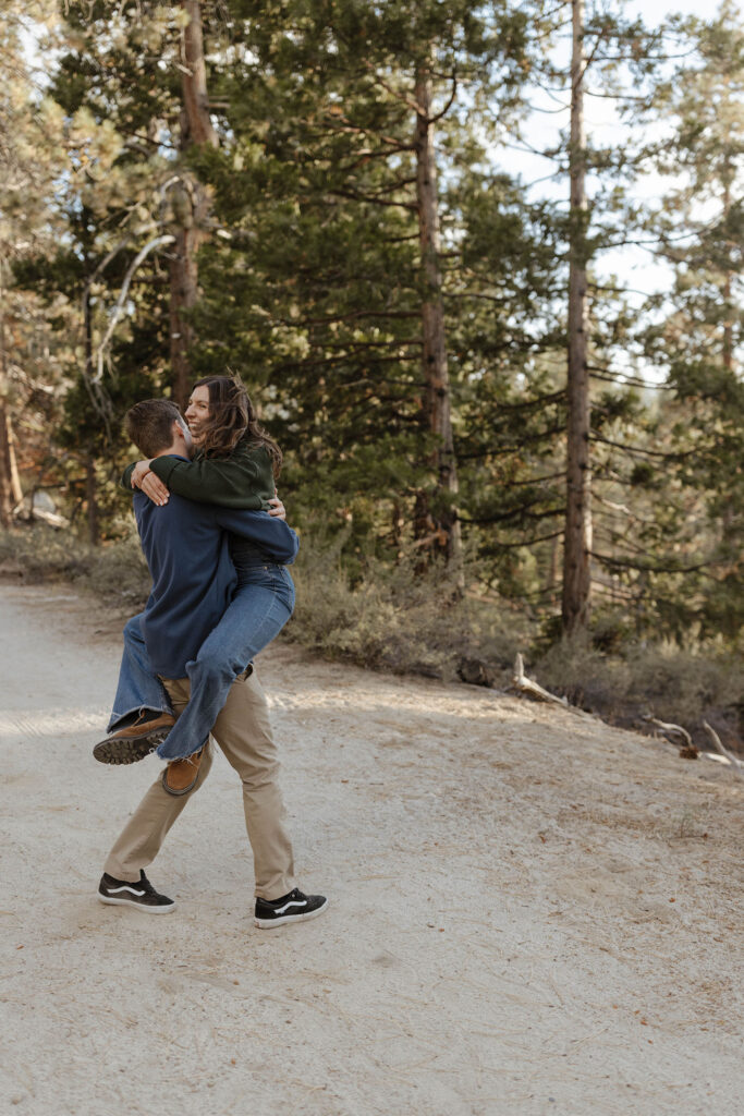 Man holding and carrying fiancé as she laughs and holds on while on trail in Lake Tahoe