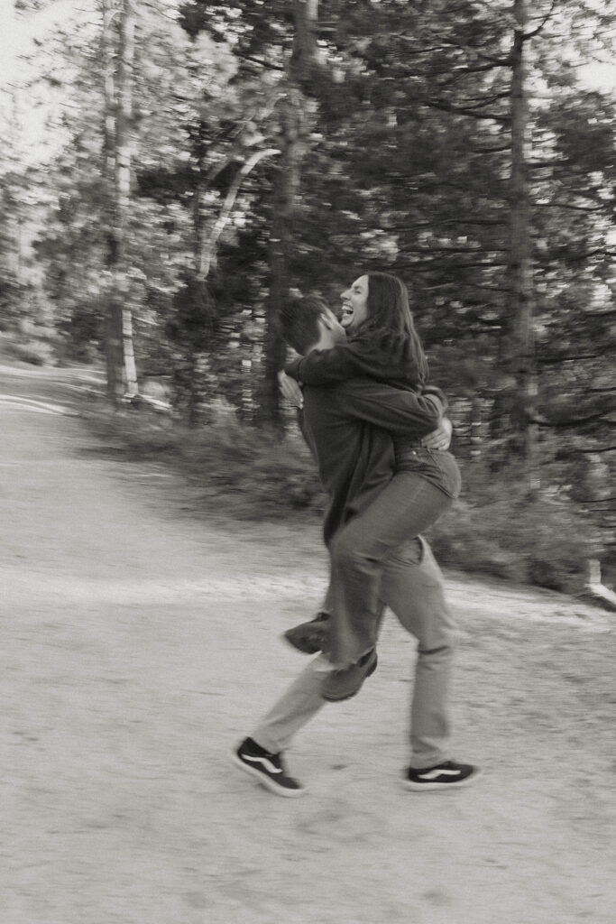 Woman laughing as fiancé carries her across trail in Lake Tahoe