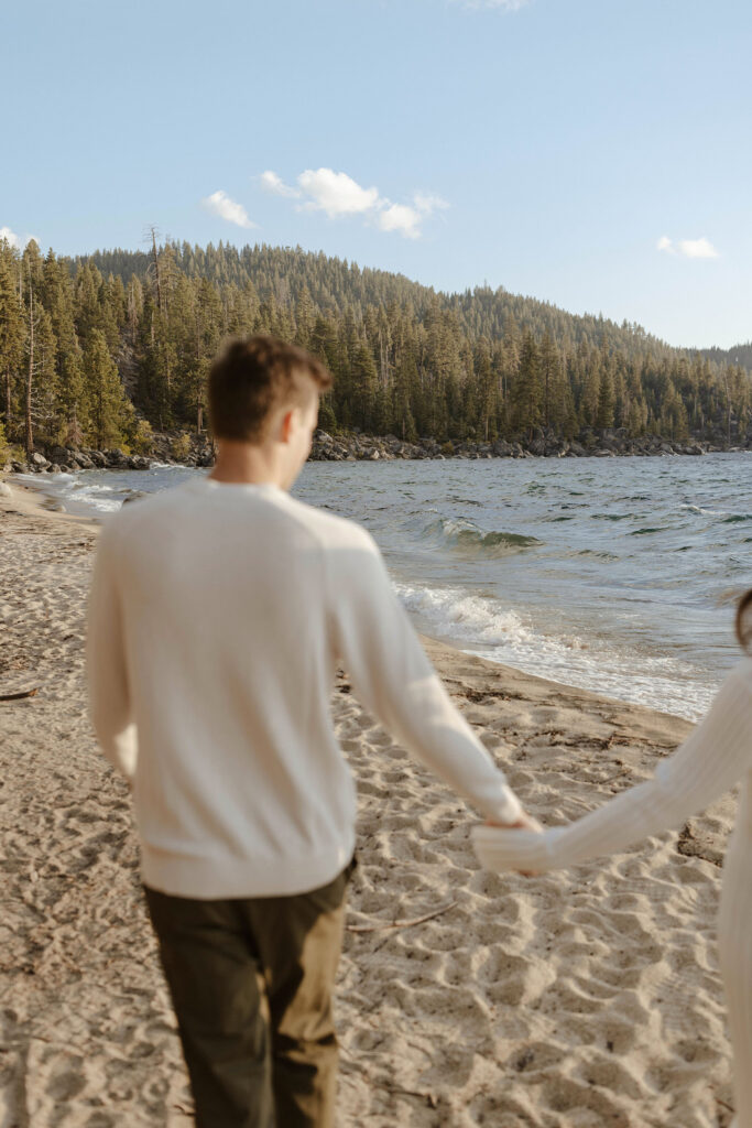 Engagement couple walking across beach together while holding hands in Lake Tahoe