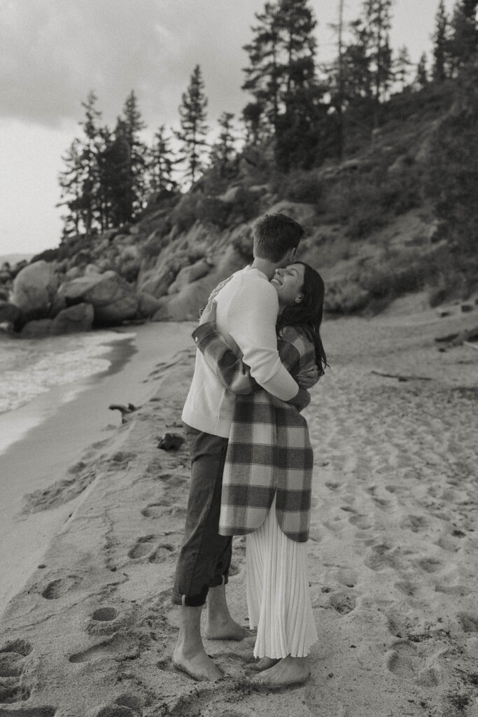 Engagement couple hugging while standing barefoot on beach together in Lake Tahoe