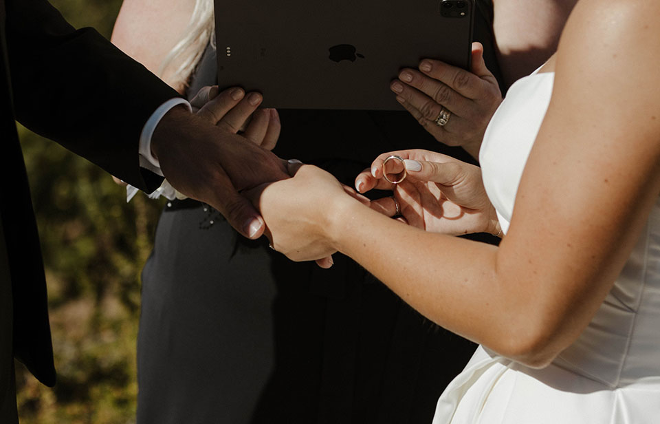 Bride holding groom's hand and about to put wedding ring on his finger during ceremony at Willow Heights mansion