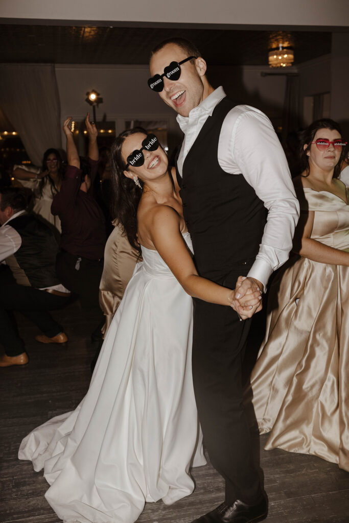 Wedding couple dancing together while laughing and wearing "bride" and "groom" glasses during reception at Willow Heights mansion