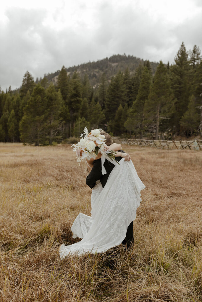 Wedding couple hugging while bride holds floral bouquet and dress up while in golden field at the PlumpJack Inn