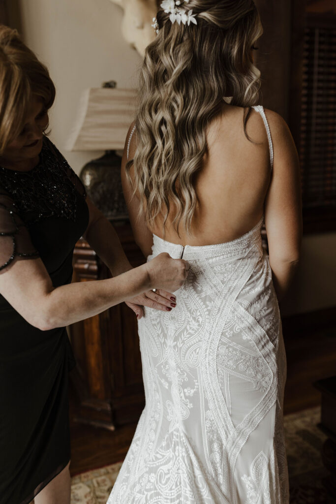 Bride's mom fastening back of wedding dress while bride is getting ready inside at the PlumpJack Inn
