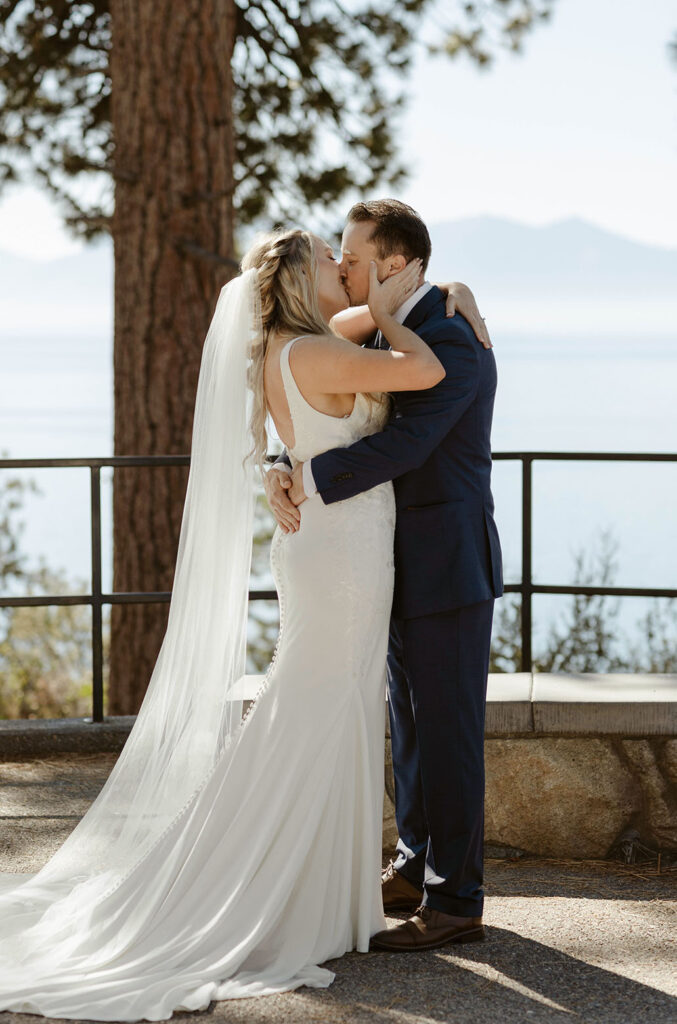 Wedding couple kissing while holding each other after ceremony at Logan Shoals with Lake Tahoe and mountains in background