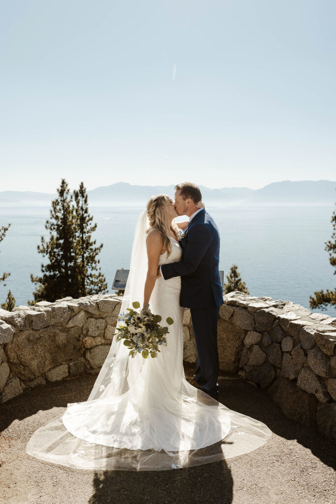 Wedding couple kissing while holding each other in front of rock wall at Logan Shoals with Lake Tahoe and mountains in background