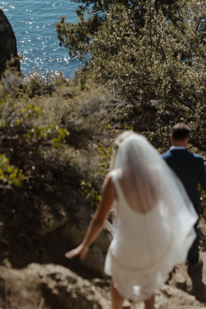 Wedding couple walking down steep rocky trail together towards water at Logan Shoals