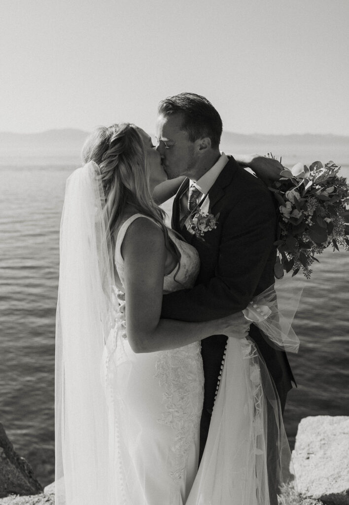 Wedding couple kissing while holding each other with Lake Tahoe directly behind them at Logan Shoals