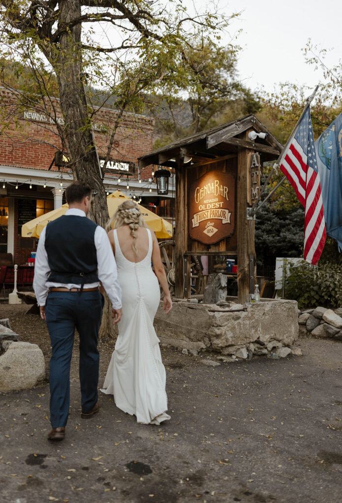 Wedding couple walking together up to rustic brick building with wooden Genoa Bar sign next to them at Logan Shoals