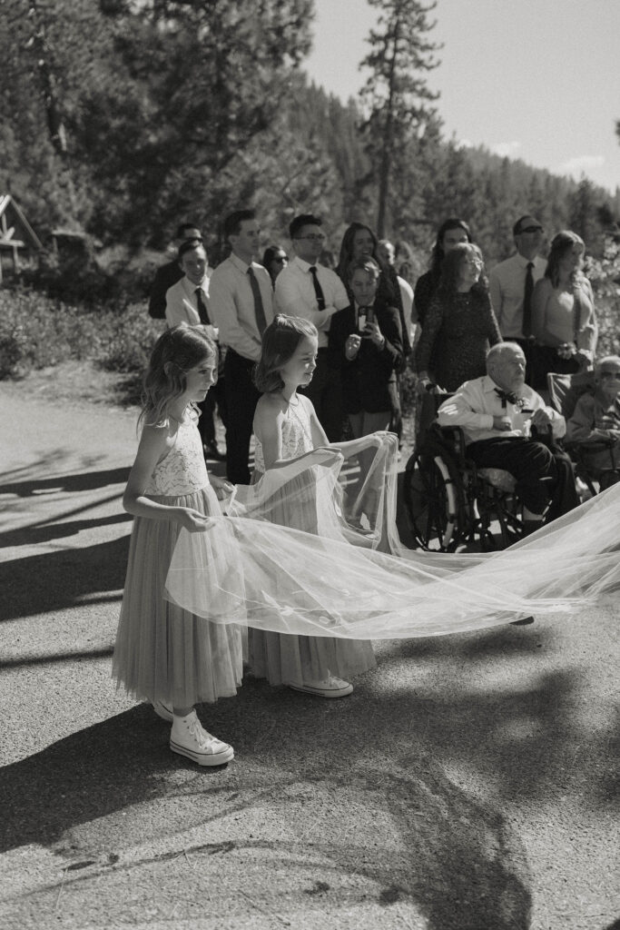 Little girls in bridesmaid dresses holding bride's wedding veil as she walks down aisle during ceremony at Logan Shoals