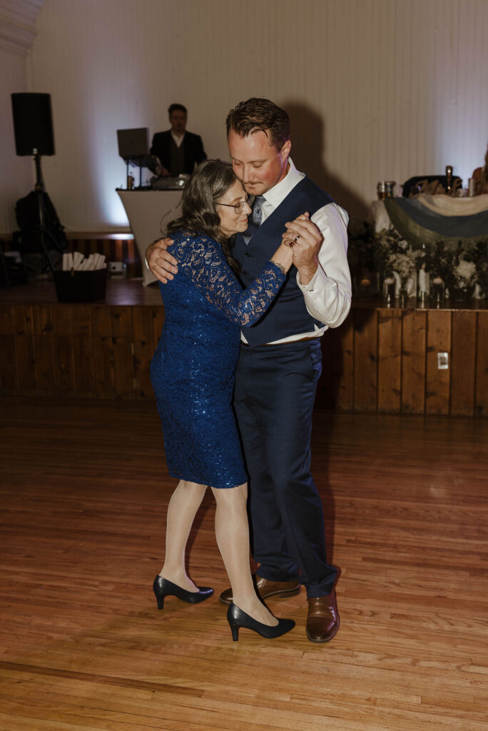 Groom dancing with his mom while holding her hand during wedding reception at Logan Shoals with band in background