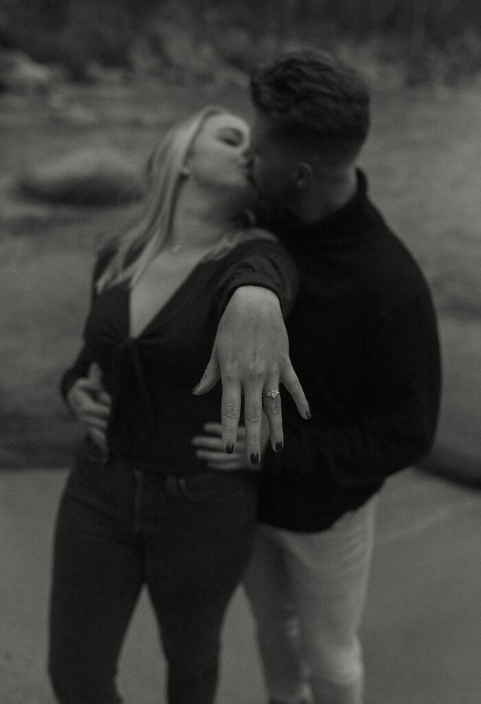 Woman showing off engagement ring on finger while kissing fiancé and standing on a beach in Lake Tahoe