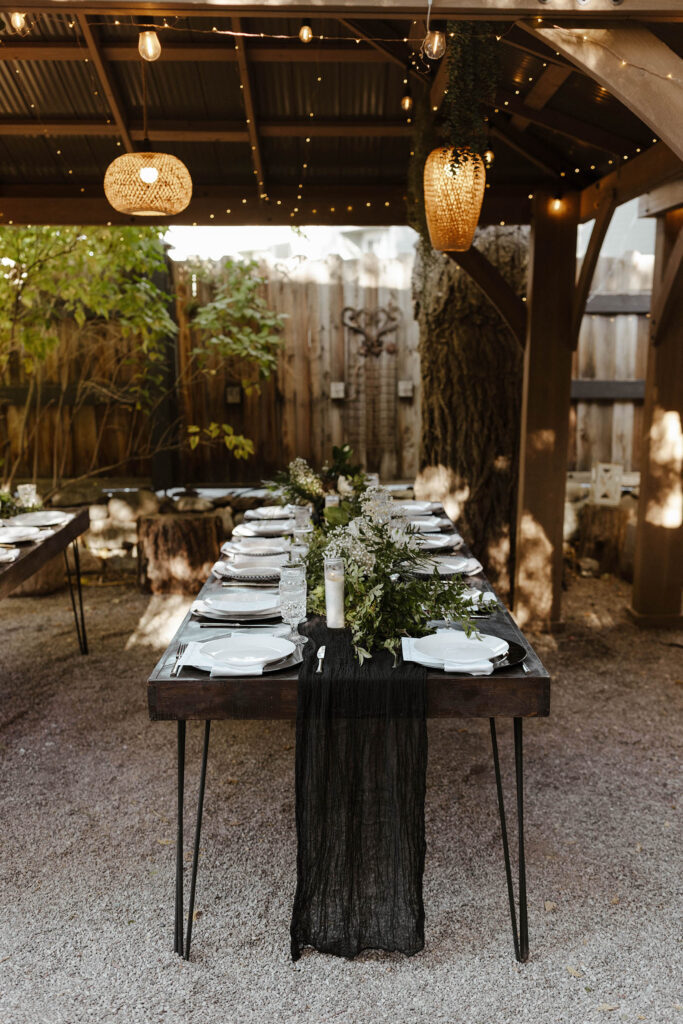 Wedding reception dinner table with green florals and black decor with hanging wicker lights above at Sierra Water Gardens
