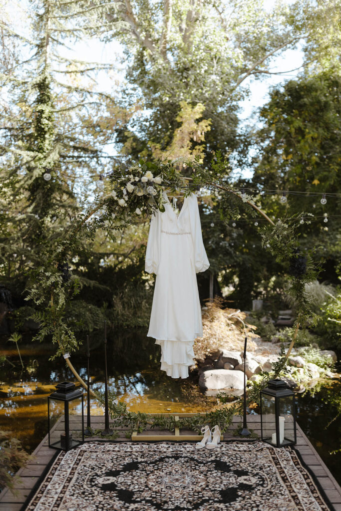 Bride's wedding dress hanging from ceremony arch in front of pond with garden at Sierra Water Gardens