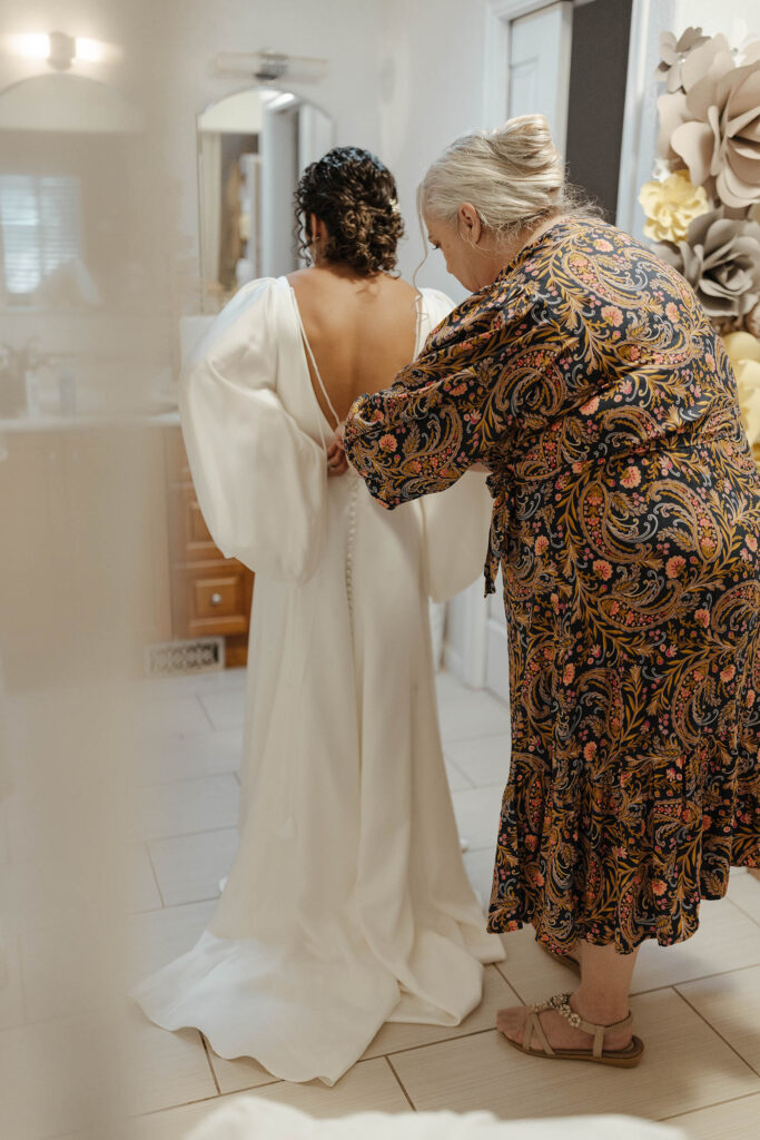 Bride's mom buttoning back of wedding dress while inside at Sierra Water Gardens