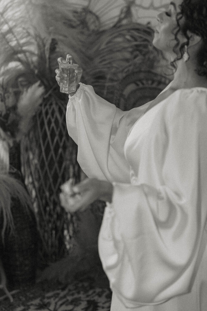 Bride applying perfume while wearing wedding dress inside at Sierra Water Gardens