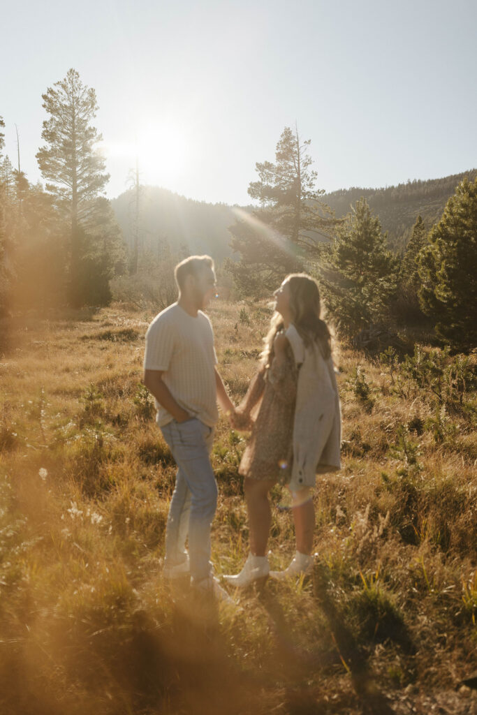 Engagement couple holding hands and standing in golden field talking to each other at Lake Tahoe with mountains in background