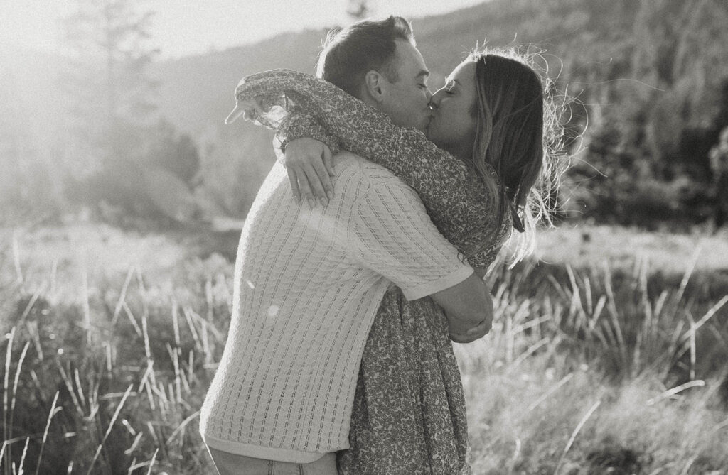 Engagement couple kissing while hugging in golden field together with trees in background at Lake Tahoe