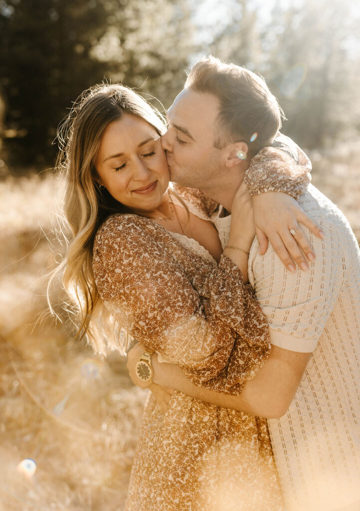 Man kissing fiancé on cheek while her eyes are closed in Lake Tahoe
