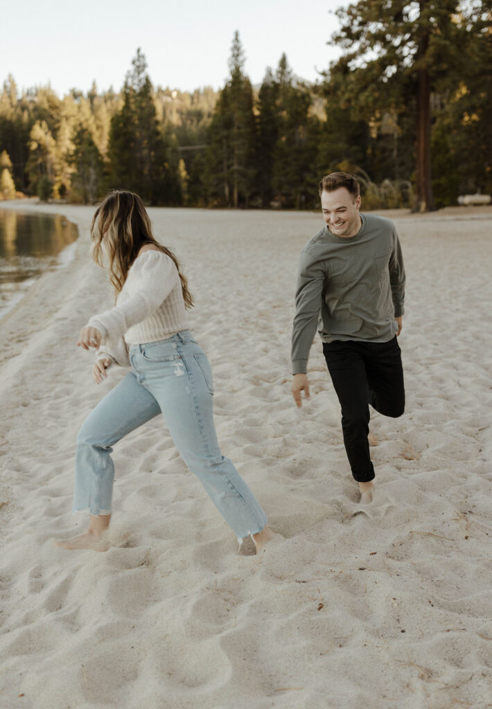 Man chasing after fiancé while laughing on a sandy beach in Lake Tahoe