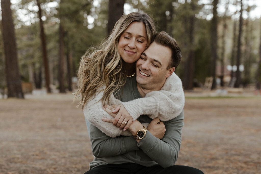 Engagement couple hugging each other while smiling and holding hands in Lake Tahoe with trees in background