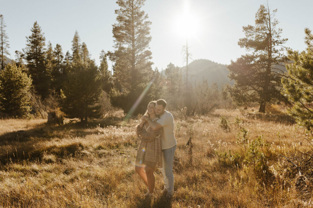 Man hugging fiancé from behind while standing together in golden field with tress in background at Lake Tahoe
