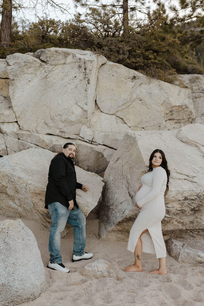 Couple leaning on large rocks together while pregnant woman holds belly and husband looks at camera in Lake Tahoe
