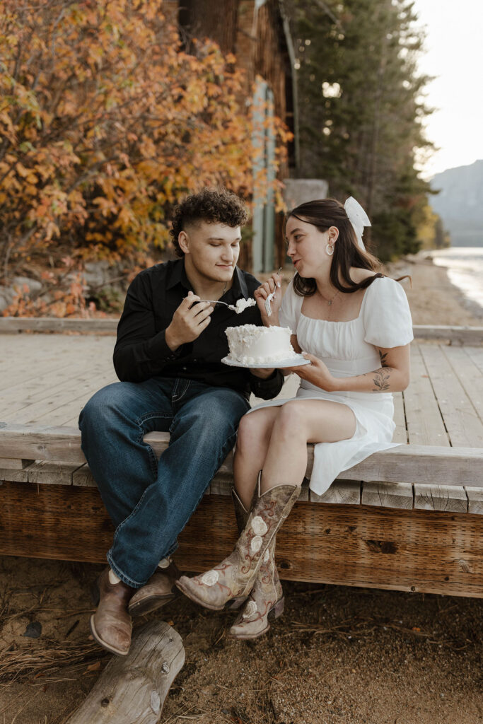 engagement couple sitting on a dock in south lake tahoe, eating a vintage wedding cake