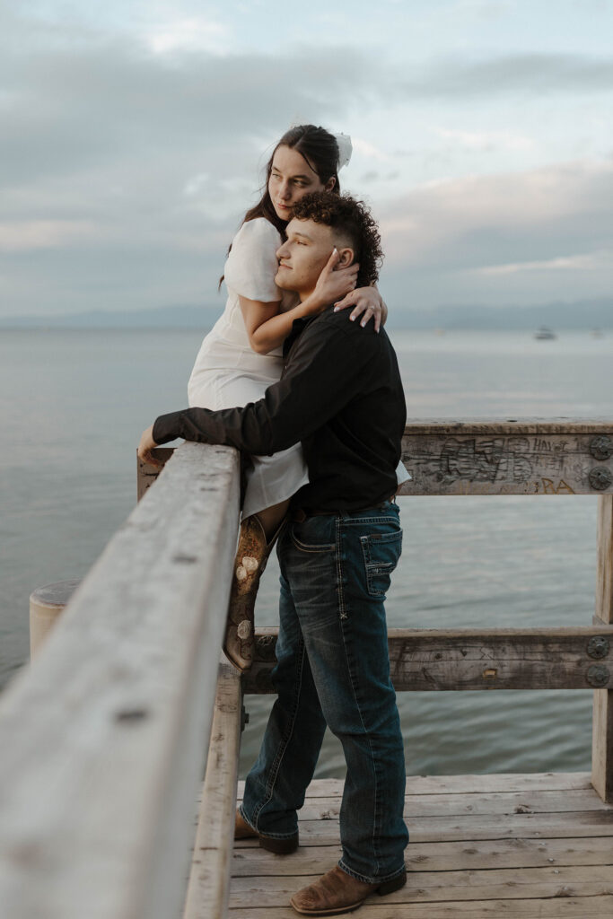 woman sitting on the side of a dock in south lake tahoe, holding her man as they look out at the water