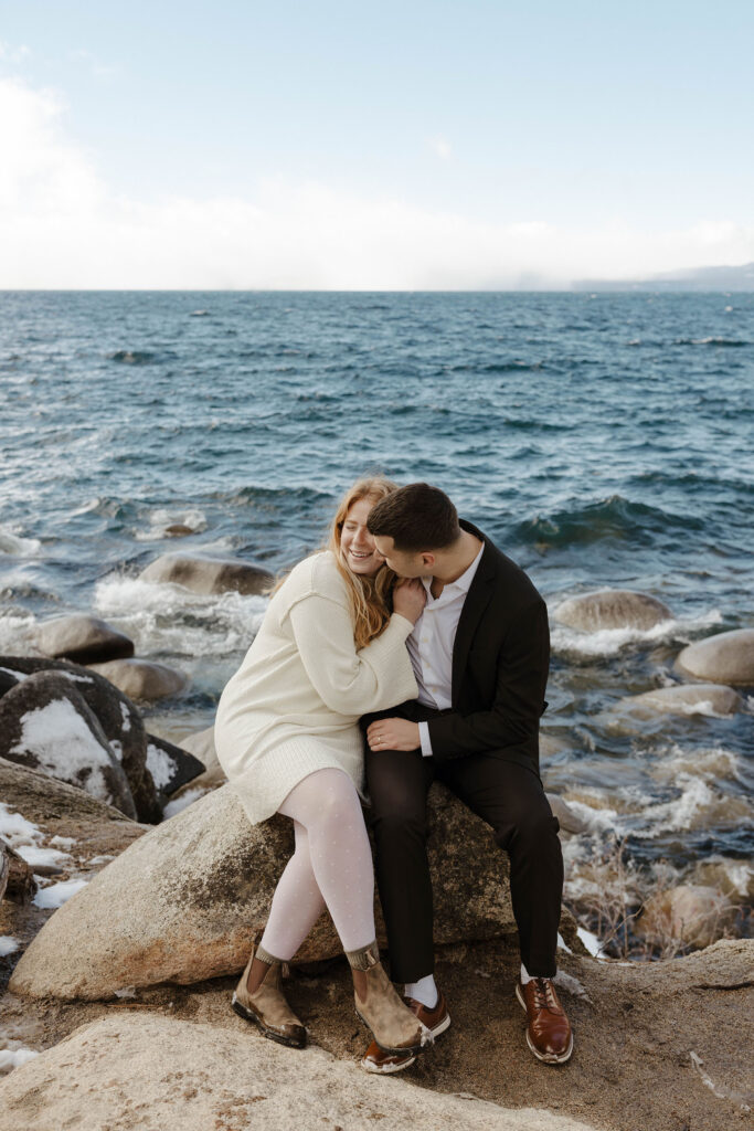 couple sitting on a rock and hugging by the water in lake tahoe