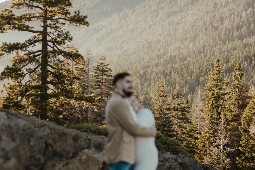 couple hugging at eagle rock in lake tahoe, withe the forest in focus behind them