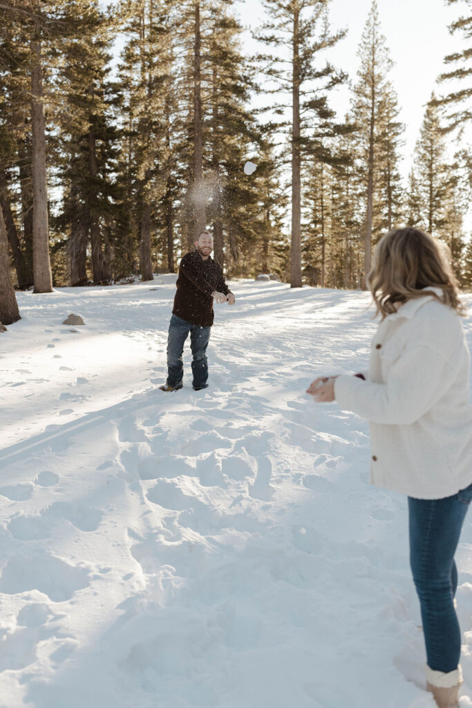 Man throwing snowball at wife while in the snow in Lake Tahoe with pine trees in background