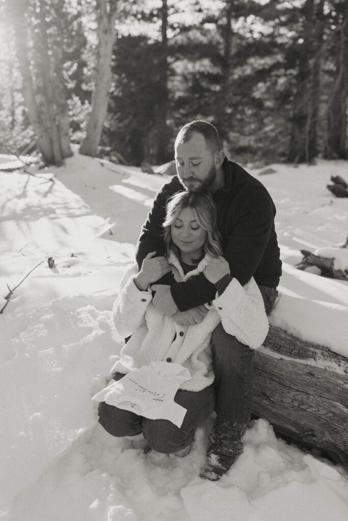 Man hugging wife from behind while sitting on large log with snow all around in Lake Tahoe