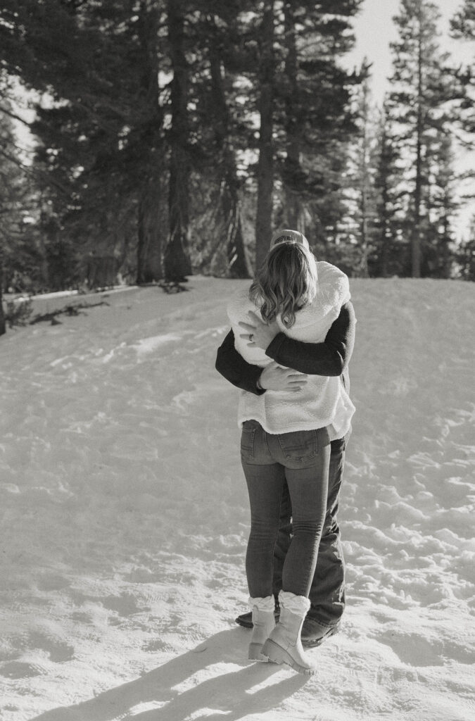 Couple hugging each other while standing in the snow with pine trees in background at Lake Tahoe