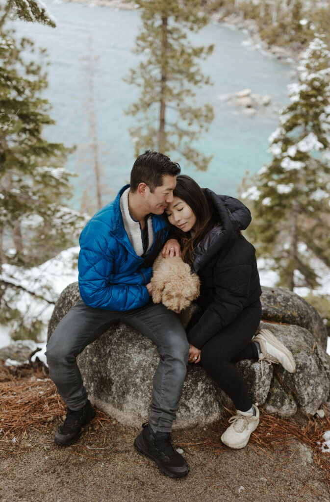 couple sitting on a rock in lake tahoe holding their dog