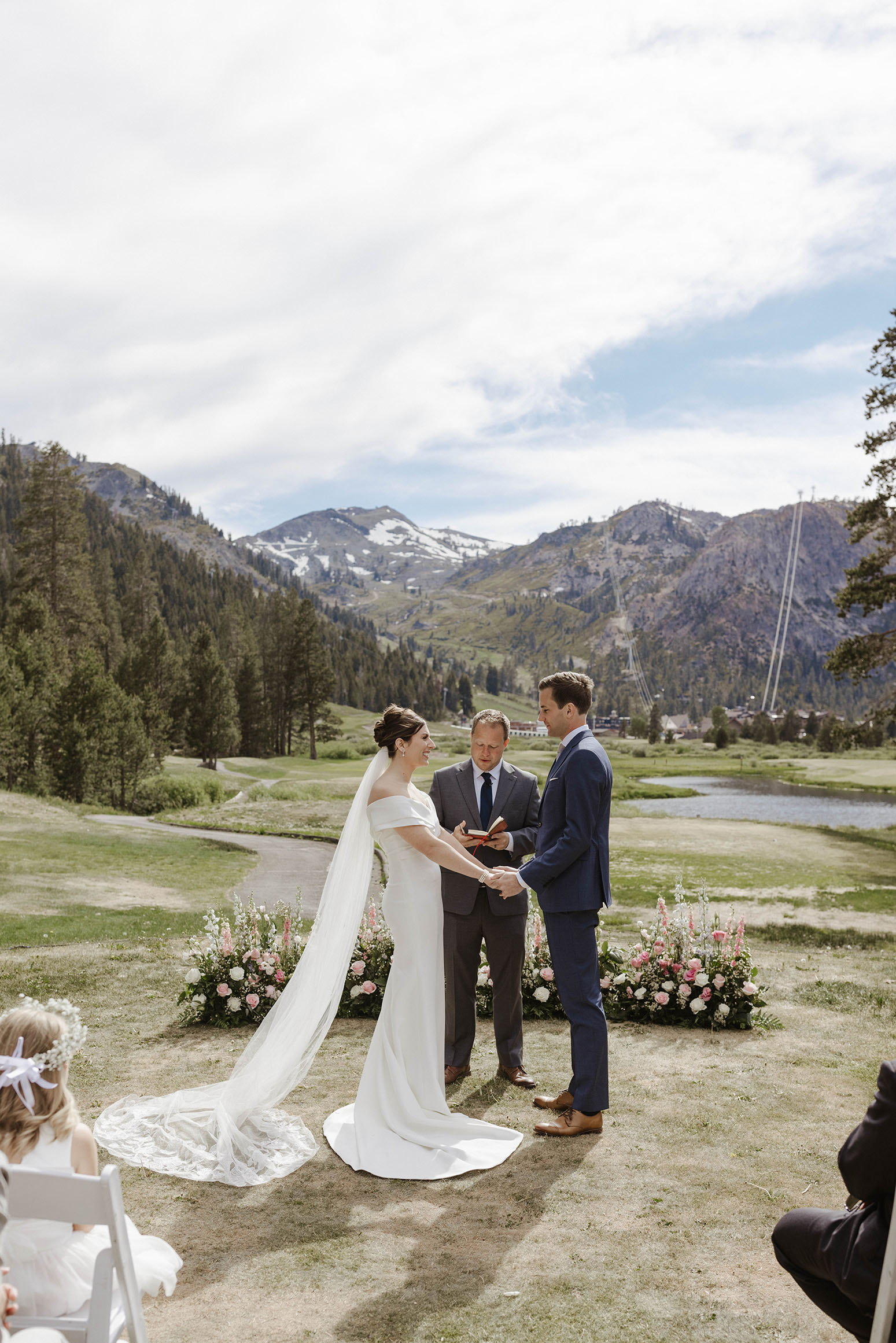 Wedding couple holding hands during ceremony at Everline Resort with pink and white floral arrangements and green mountains in background