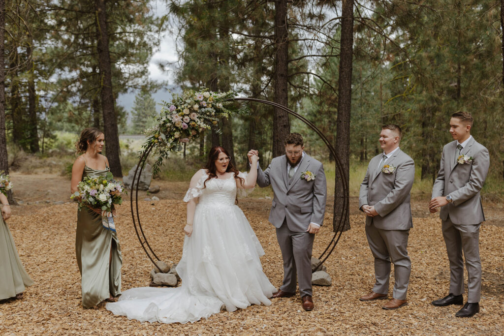 bride and groom holding hands in the air during ceremony at the corner barn in graeagle