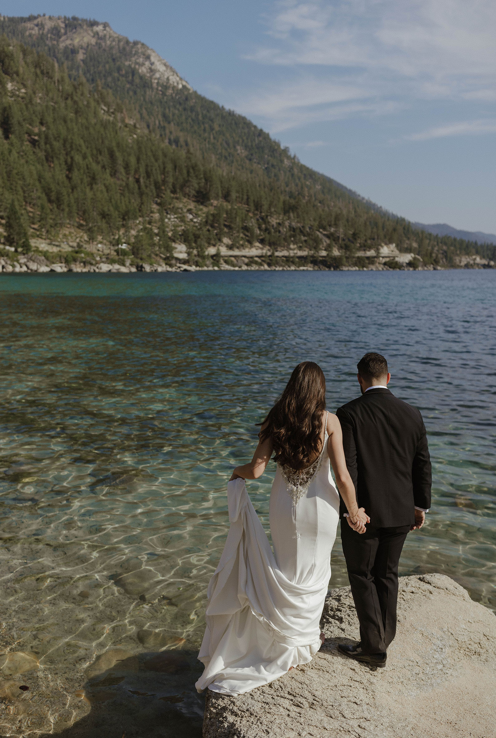 wedding couple walking on a rock with Lake Tahoe's clear blue water below them