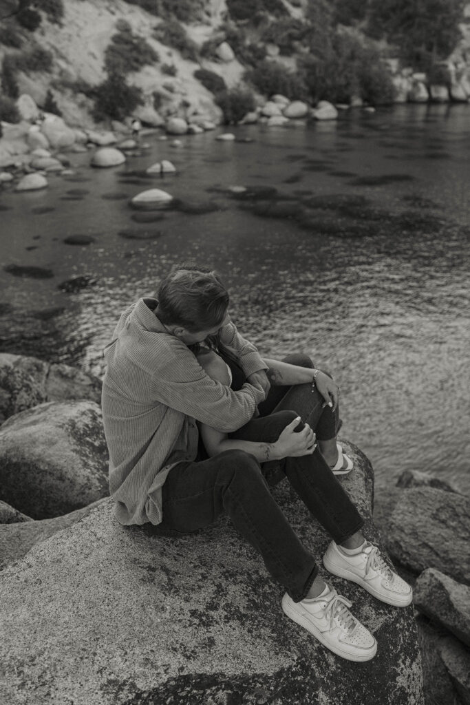 couple sitting on a rock in lake tahoe hugging each other