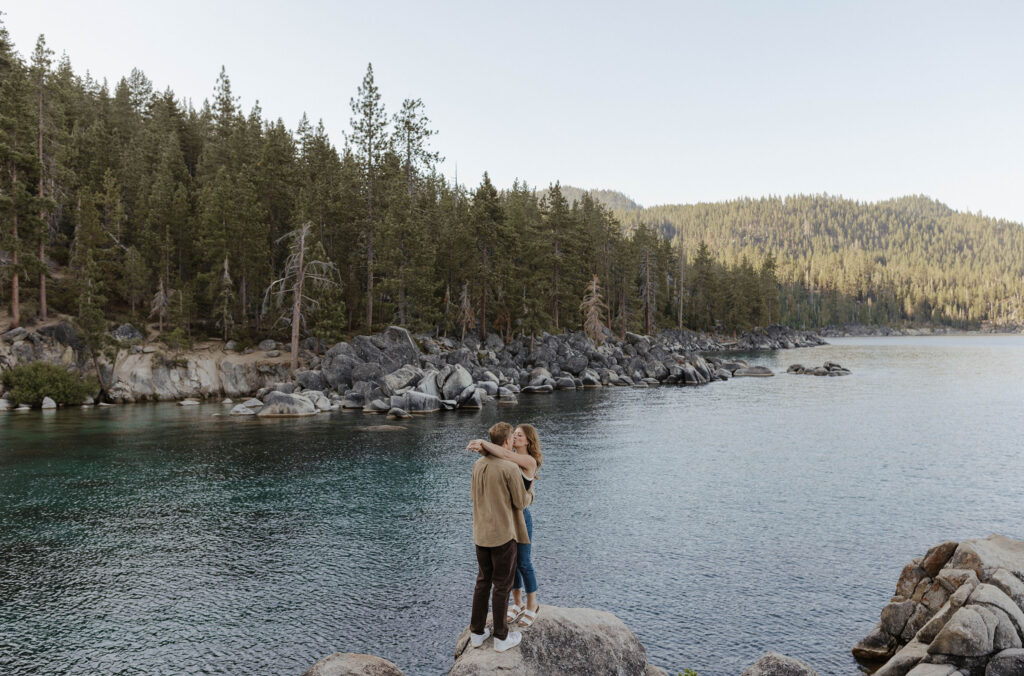 couple kissing while standing on a rock in lake tahoe in the distance